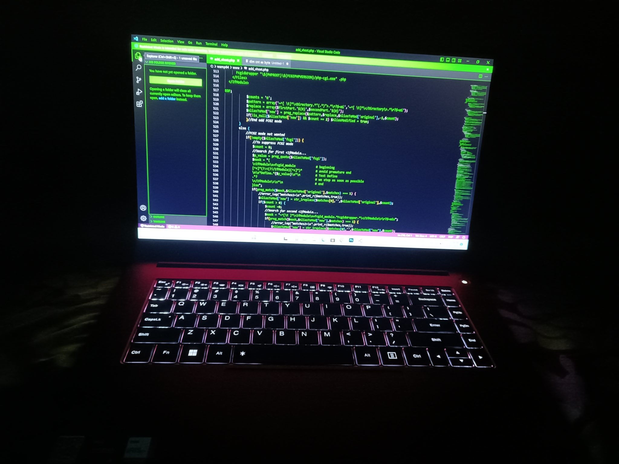 Portátil con teclado retroiluminado y código en pantalla, en una sala en penumbra